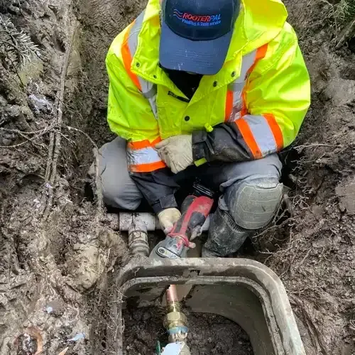 A RooterPAL plumber in a high-visibility jacket and cap works on underground pipes, with a new water meter and valves visible in the foreground.